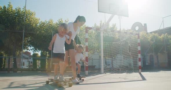 Mother Teach Her Children to Ride on Skate and Longboard on Summertime Vacation alt