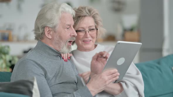 Happy Old Couple Sitting on Sofa and Using Tablet alt