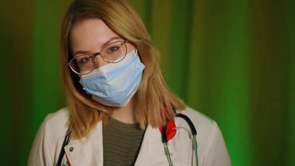 Young Nurse in Face Mask and Glasses Looking at you During Home Visit alt