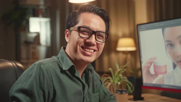 sian Male Editor Works In Photo Editing Software. He Turns And Warmly Smiles Into The Camera alt