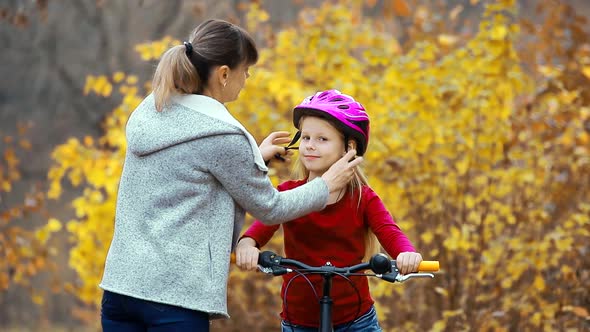 Mom helps the girl to put on a safe helmet before riding a bike on a Sunny autumn day in nature  .