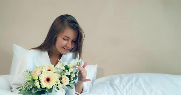 Pretty Woman Holds Nice Flowers Bouquet Sitting on Soft Bed