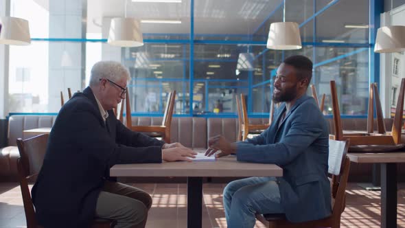 Side View of Business Partners Sign Contract and Shake Hands in Empty Restaurant alt