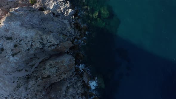 Slow Overhead Top Down Aerial Along Generic Rocky Coast with Turquoise Water and Waves Crashing alt