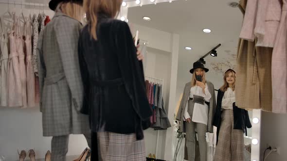 Trendy Joyful Young Women Taking Selfie in Fitting Room Against Big Mirror of Modern Boutique alt