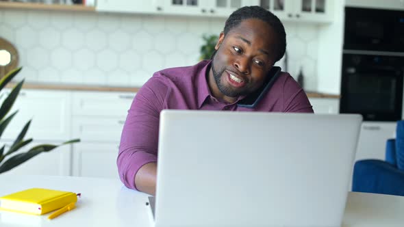 Positive AfricanAmerican Man Talks on the Smartphone Typing on the Laptop alt