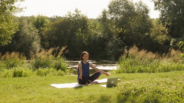 Practicing yoga and meditating in park with laptop. alt