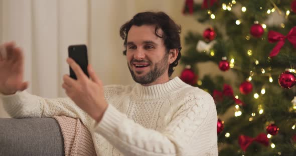 Man Celebration New Year Near Christmas Tree at Home Video Call Congratulation on Smartphone alt