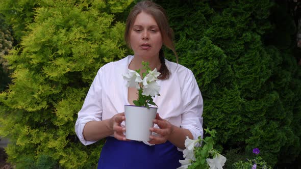 Happy Confident Woman Admiring White Flower in Pot Smelling Plant in Slow Motion Smiling alt