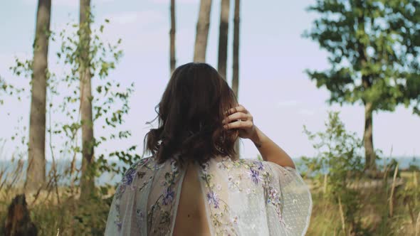 Attractive Woman with Red Lips Touches Her Curly Hair Walk in the Forest View From Back Slow Motion alt