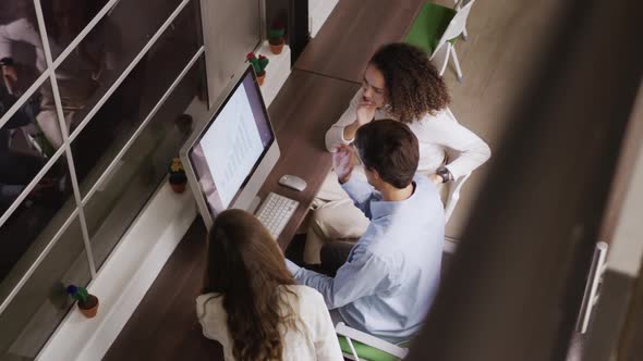Creative businesspeople discussing over computer in modern office alt