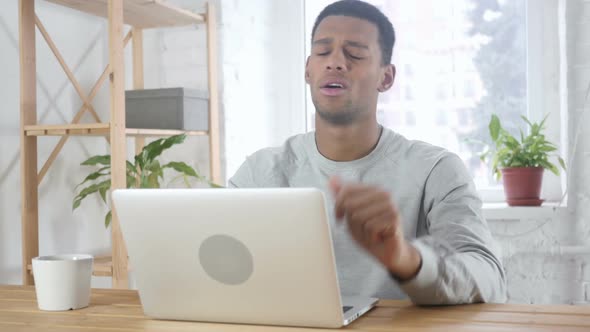 AfroAmerican Man Sitting in Office Upset By Loss Working on Laptop alt