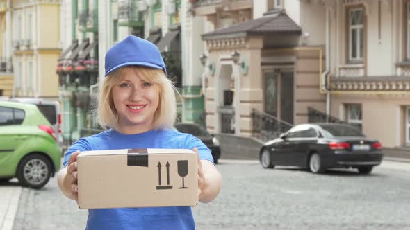 Cheerful Delivery Woman in Blue Uniform Holding Cardboard Box