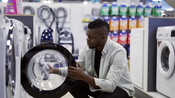 Afroamerican Man is Choosing Washing Machine in Home Appliances Store Viewing Exhibition Sample alt