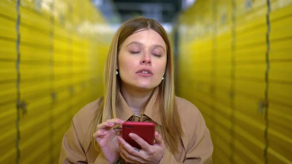 Portrait of Young Brunette Woman with Green Eyes Finding Lockers Using App on Smartphone alt