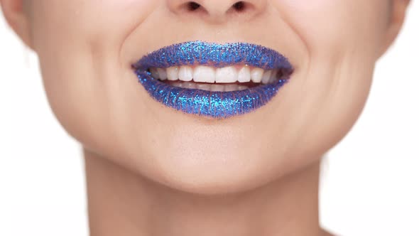 Extreme Close Up Portrait of Happy Female Lips Covered with Blue Shining Glitter Giving Air Kiss alt