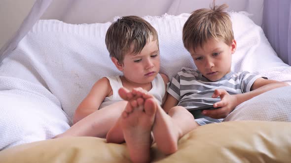  Get bored background. Two boys holding smartphone, tablet sitting on chair, focus on children feet.