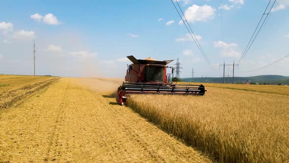 Aerial View Front View of Combine Harvester Harvesting Wheat Emits Clouds of Dust and Smoke alt