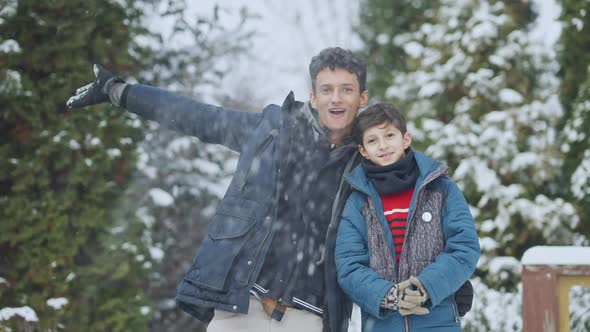Middle Shot of Positive Teenage and Little Brothers Tossing Snow in Slow Motion Looking at Camera alt