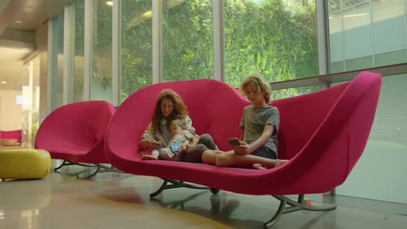 A Ukrainian Family is Sitting at the Airport in a Red Chair Waiting for Their Flight to Their alt