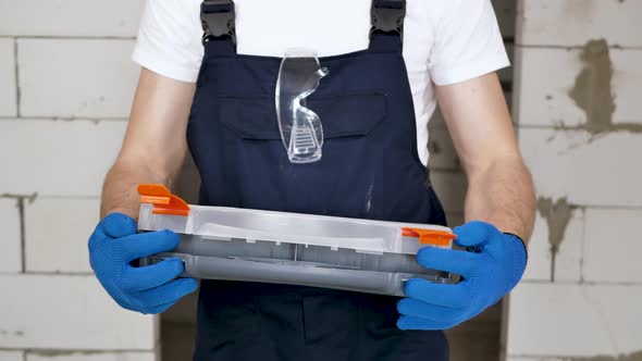 A Handsome Male Construction Worker Opens a Toolbox Against a Brick Wall alt