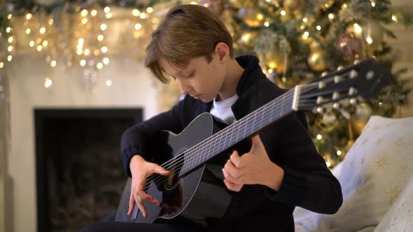 Handsome Caucasian Boy Plays Guitar Sits on Sofa Against Background alt
