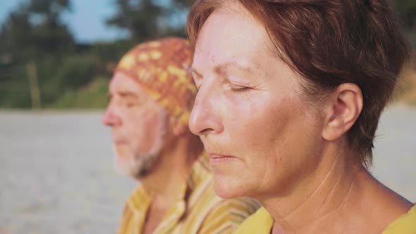 Senior Couple Sits and Meditating Together on Sandy Beach