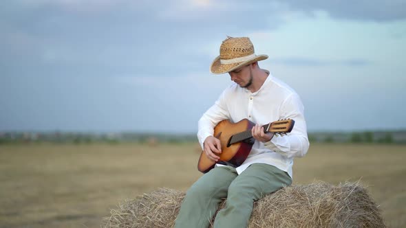 Man Wearing a Straw Hat Playing the Guitar About a Haystack alt