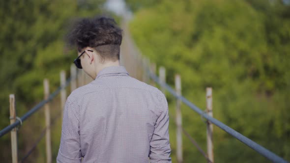 Guy Walks on Suspended Bridge in the Forest alt