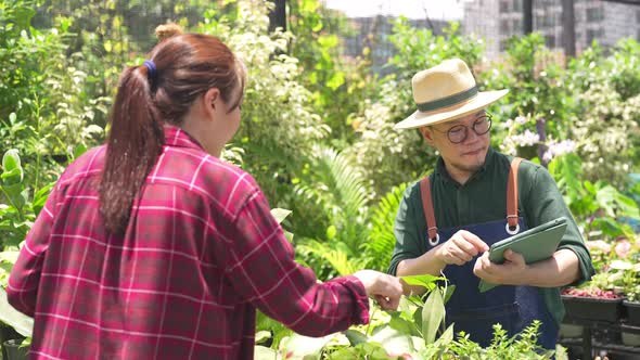 4K Asian man plant shop owner helping woman customer choosing potted plants in store alt