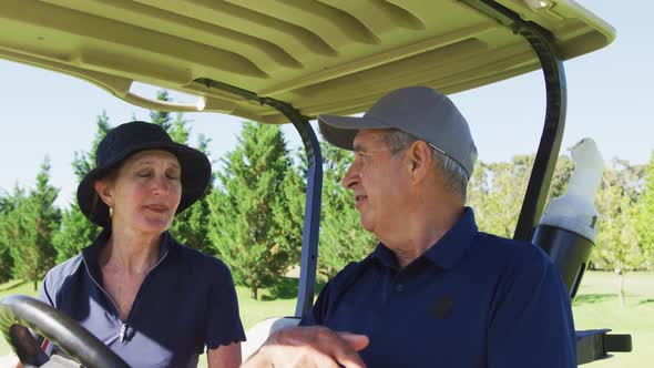 Caucasian senior couple talking to each other while sitting in the golf cart at golf course alt