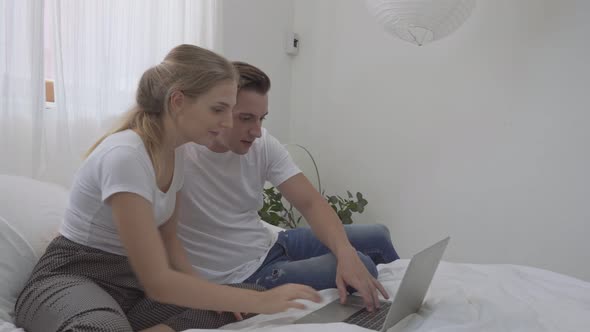 Couple working on computer laptop together on a bed
