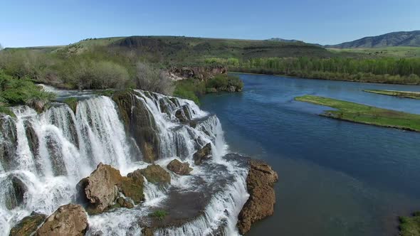 Flying view of waterfall flowing over edge into river alt