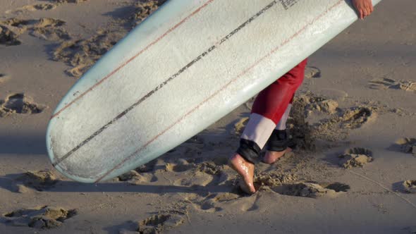 Santa Claus walking with his surfboard to go surfing at the beach. alt