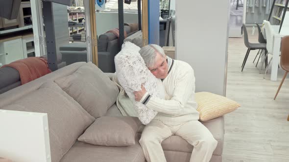 Cheerful Elderly Man Trying Soft Cushions on Sale at Furniture Store alt