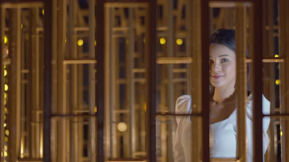 Beautiful Asian woman walking along a wall of windows with a stunning look and smmile at the camera alt