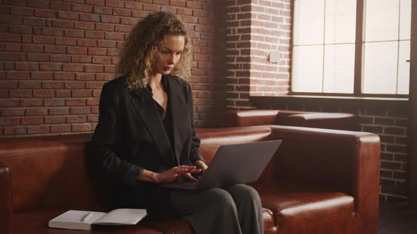 Young Stylish Businesswoman Working on a Laptop in a Loft Apartment with Red Brick Wall alt