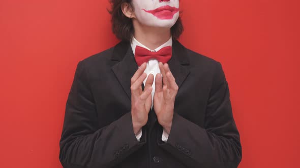 A Clown with Colorful Makeup Poses on an Isolated Red Background a Joyful Magician or a Mysterious