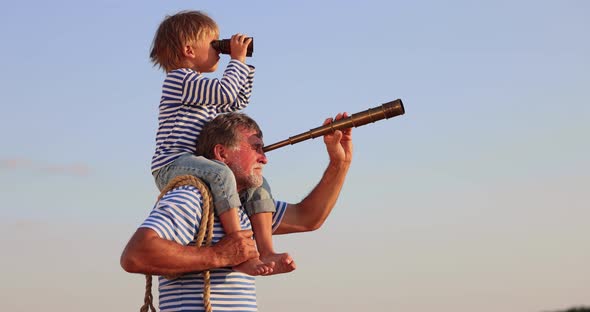 Grandfather and boy with telescope having fun outddor against blue summer sky