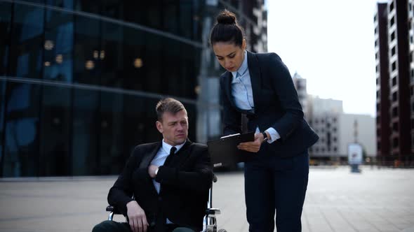 Young Cripple Business Man in Wheelchair Communicates with His Colleague About Documents Textpad alt