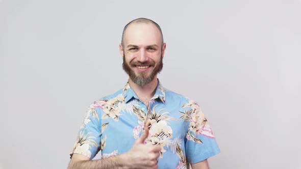 Happy bearded man wearing hawaiian shirt showing thumbs up over white background