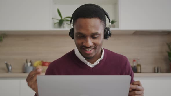 Young Afroamerican Sales Agent Celebrates a Sale with Headphones on and a Laptop in Front in His alt