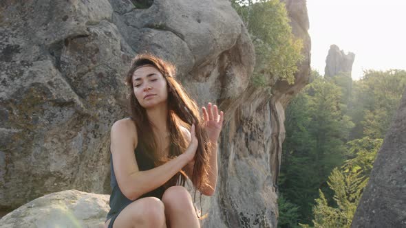 Young Woman Relaxing Outside in a Blue Silk Dress Sitting on Rocky Terrain with Mountains alt