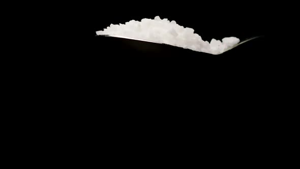 Sea Salt Falling From Spoon in Slow Motion Isolated on Black Background