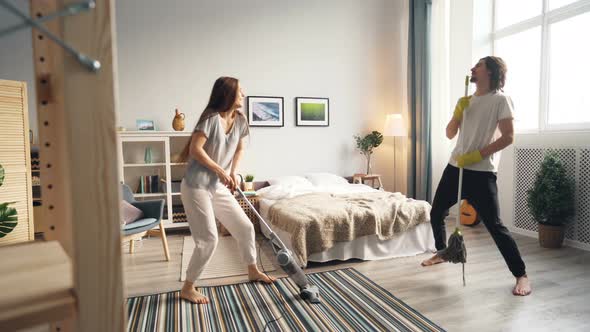 Loving Couple Cleaning Floor with Vacuum Cleaner and Mop Dancing Singing alt