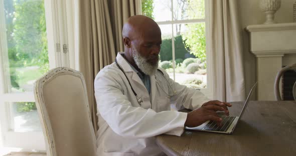 African american senior male doctor using laptop at home alt