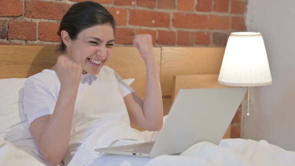 Young Indian Woman Celebrating Success on Laptop in Bed alt