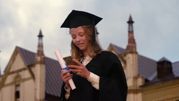 Pretty Teen in Graduation Gown Texting on Cell Phone alt
