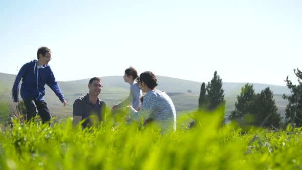 A family with 4 children having a picnic outdoors on a green hill in the sun alt