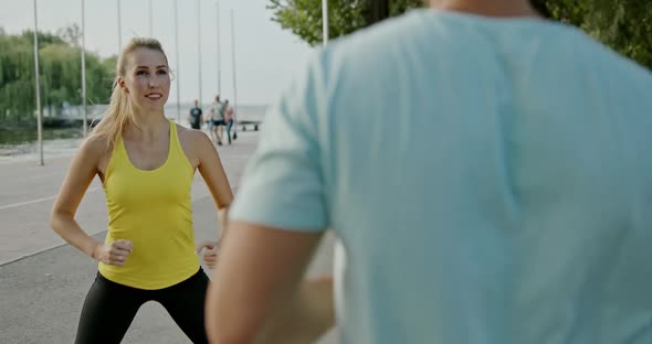 Young Couple Working Out Together in Town on an Outdoor Promenade Doing Jumps and Squats in a Health alt